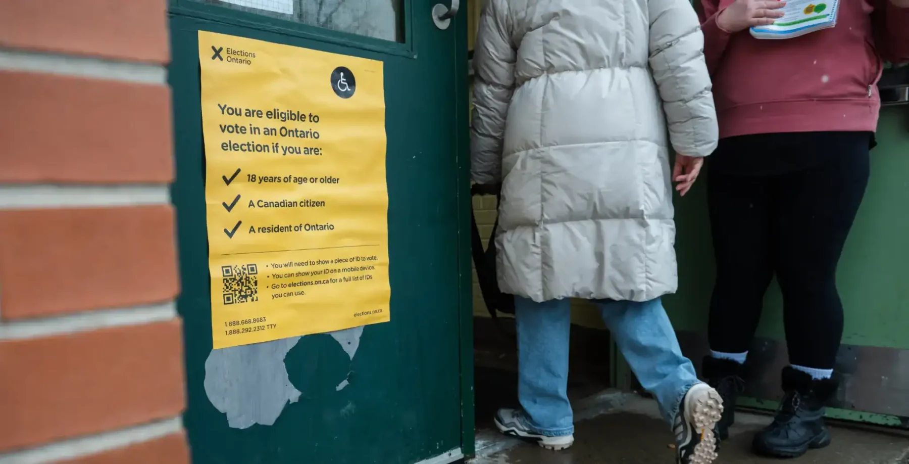 People standing near a green door with a yellow voting sign in Ontario, Canada, during an election day, focusing on civic participation and voting process.
