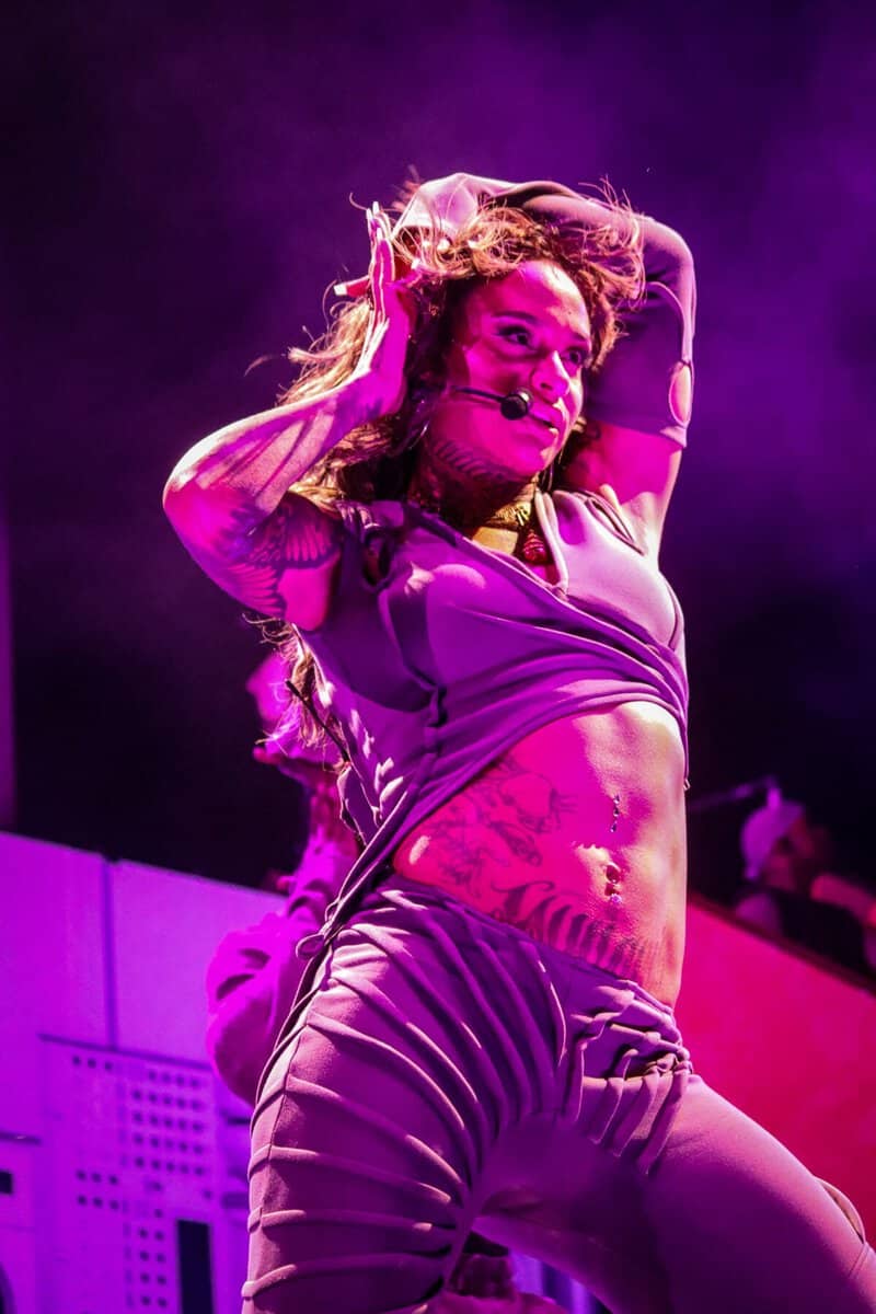 Performer on stage with purple lighting, wearing a crop top and striped pants, expressing a dynamic and energetic dance move during a concert in Toronto.