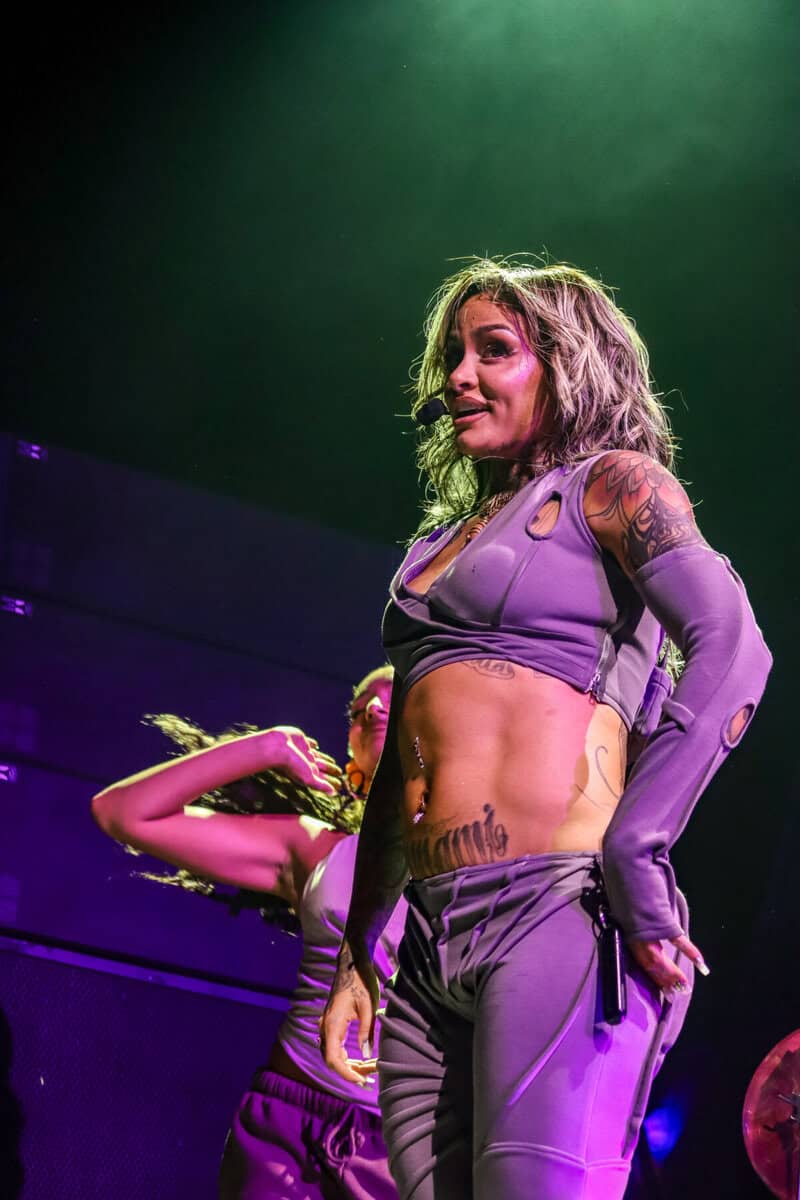 Kehlani performing on stage in Toronto, wearing a purple outfit with tattoos visible, under green and purple stage lighting.