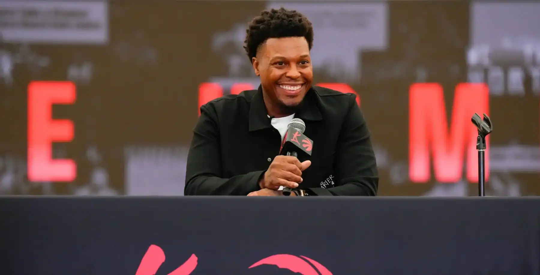 Kyle Lowry smiling at a press conference with a microphone, celebrating his jersey retirement in Toronto.