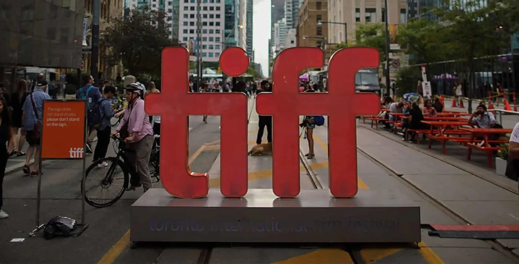 Large red 'tiff' sign on a busy city street with pedestrians and cyclists in Toronto, Canada, during daytime.