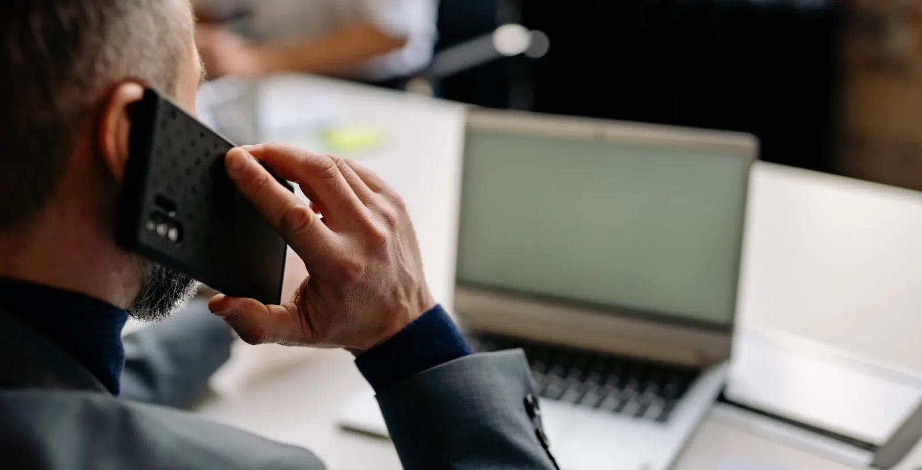 Person using a cellphone in an office setting with a laptop open on the desk.