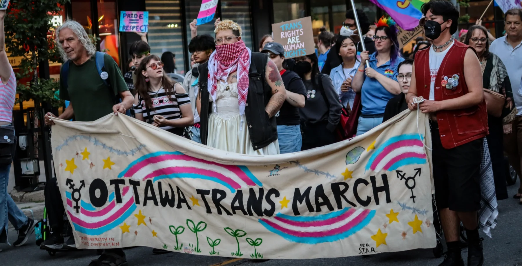 Ottawa Trans March participants holding a banner with rainbow symbols and the event name, advocating for queer and trans rights.