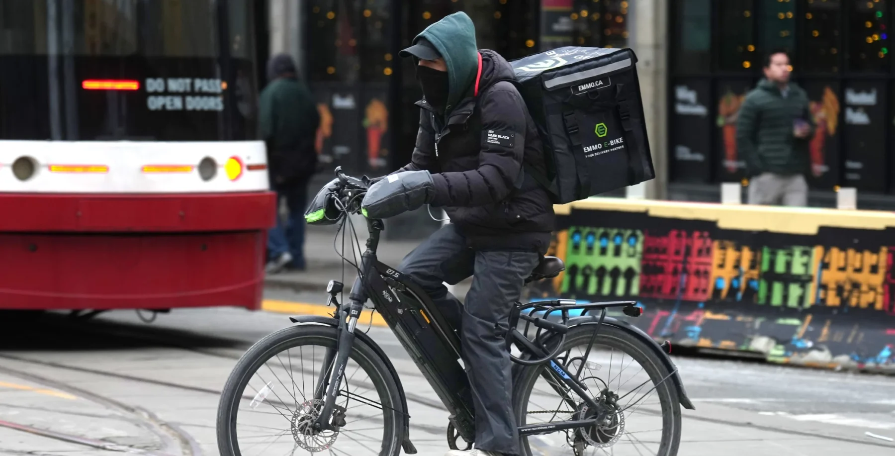 Toronto delivery person riding an e-bike with a large insulated delivery box in a busy city street.