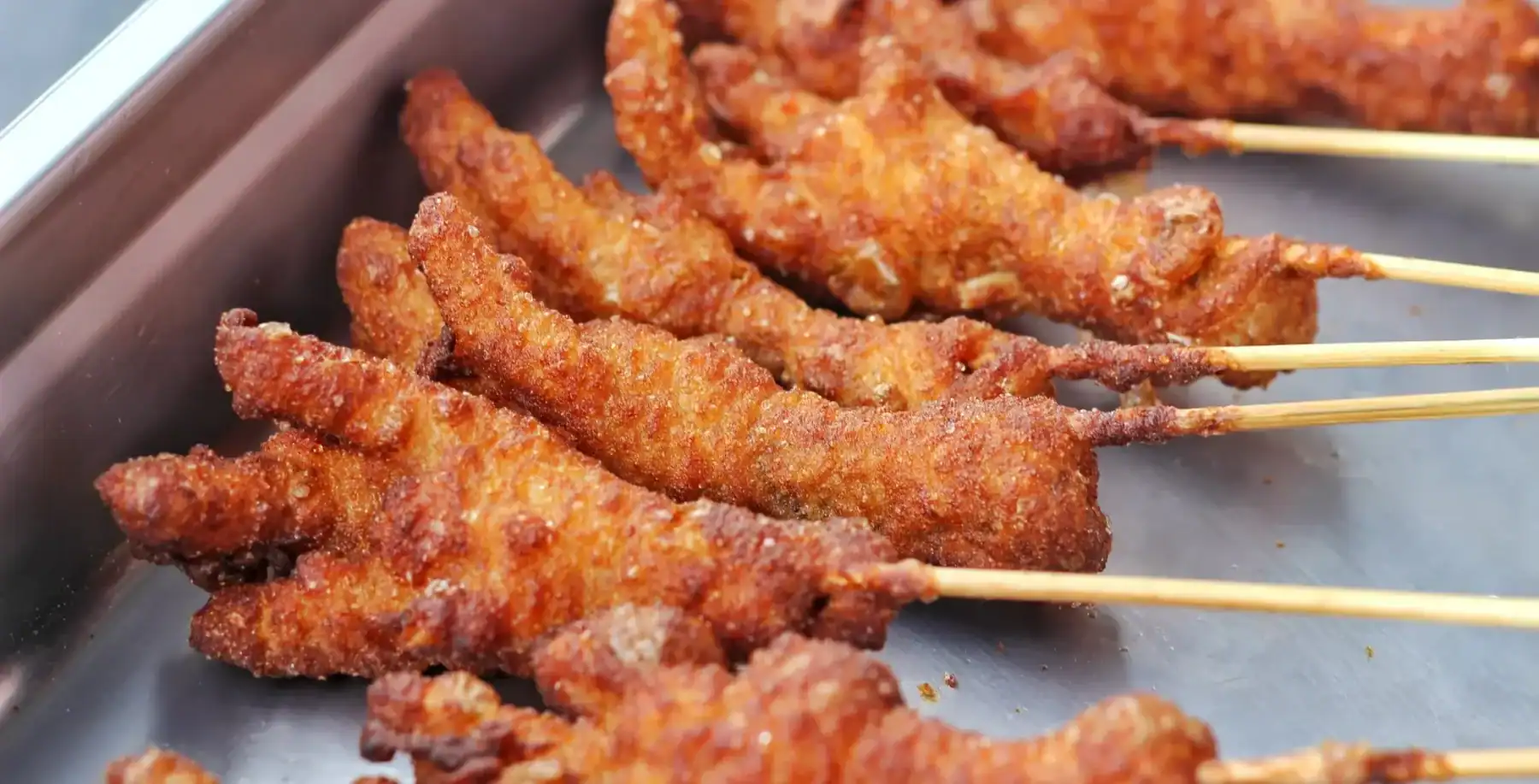 Close-up of crispy, golden-brown chicken skewers on a metal tray, ready to be served at a food event or restaurant in Toronto.
