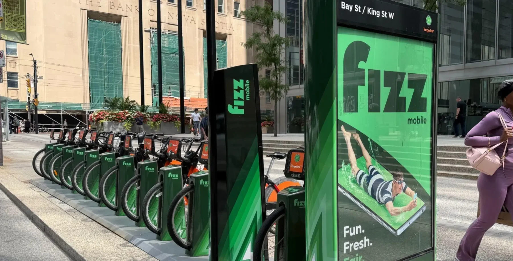 Fizz mobile phone rental station with bikes in Toronto, featuring a digital ad and city street background.