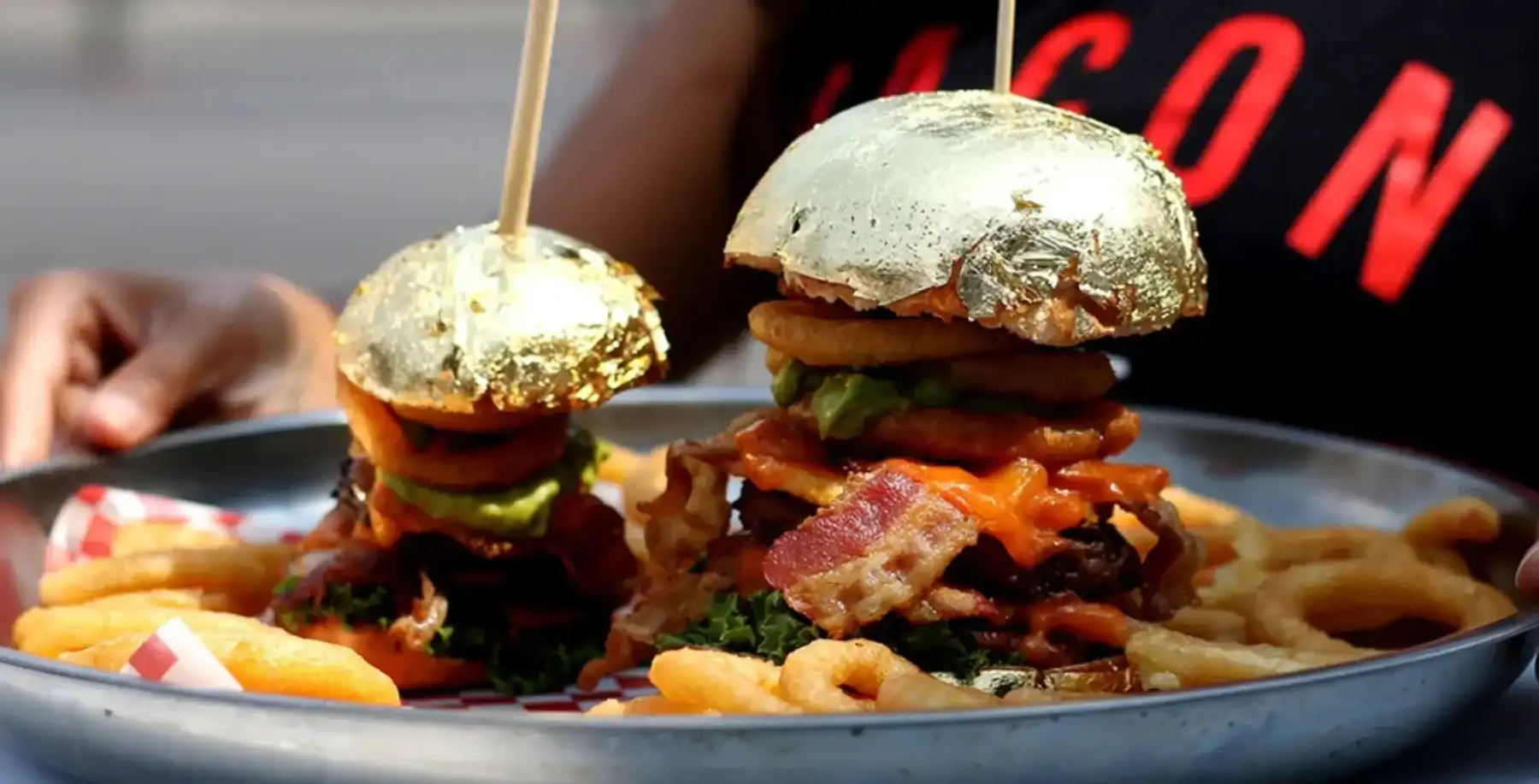 Close-up of two gourmet burgers with bacon, lettuce, tomato, and pickles served with fries on a plate, showcasing delicious comfort food.