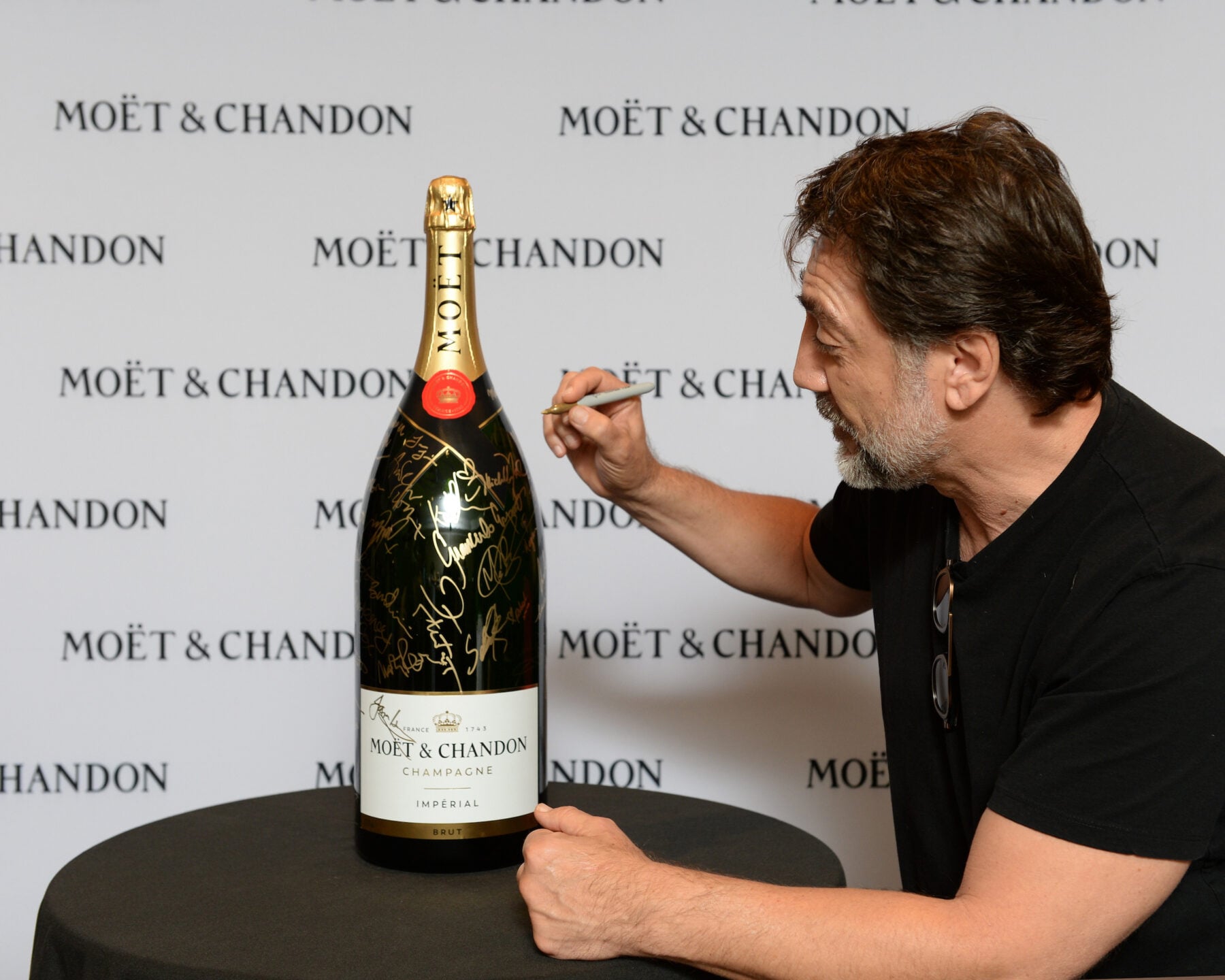 Celebrity signing a large Moët & Chandon champagne bottle at TIFF event, with branded backdrop in the background.
