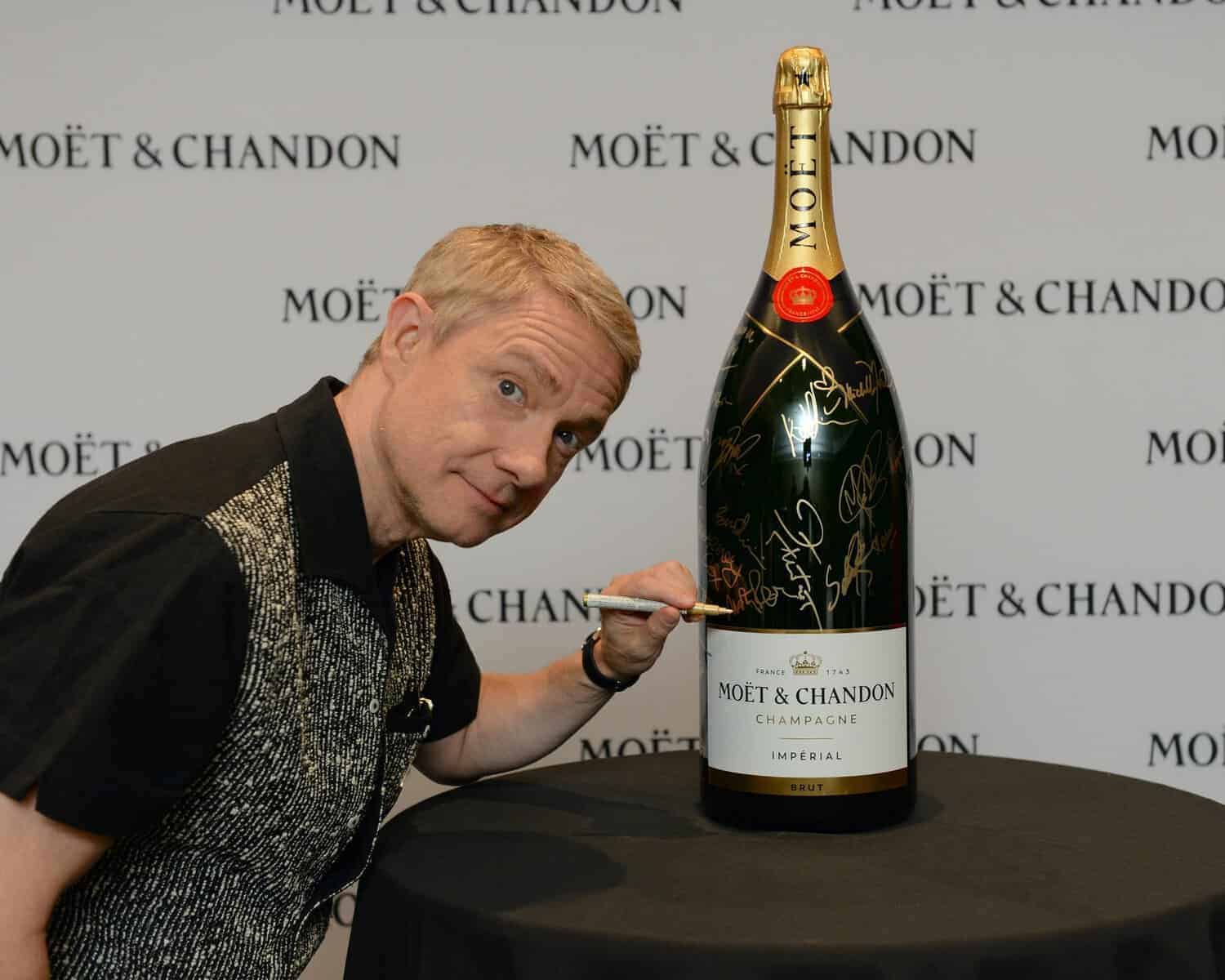 Man posing with a giant signed Moët & Chandon champagne bottle at TIFF event, celebrating celebrity signatures on the signature 9-litre bottle.