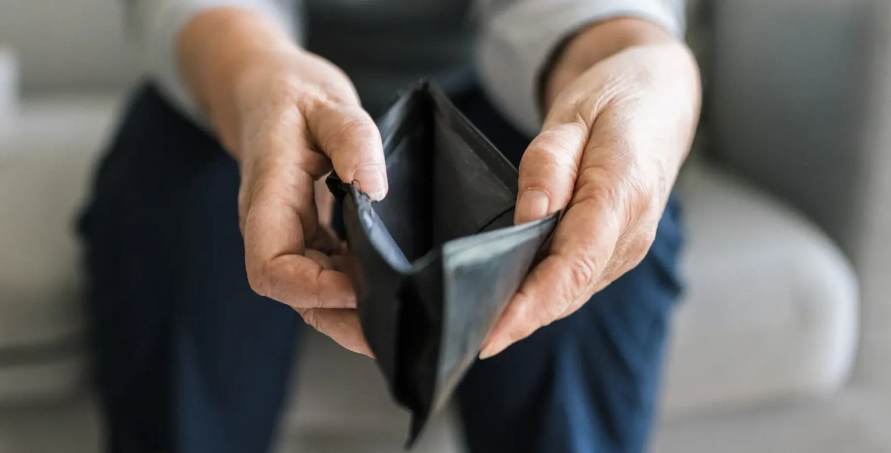 Person holding an empty black wallet, symbolizing financial dependence or lack of money.