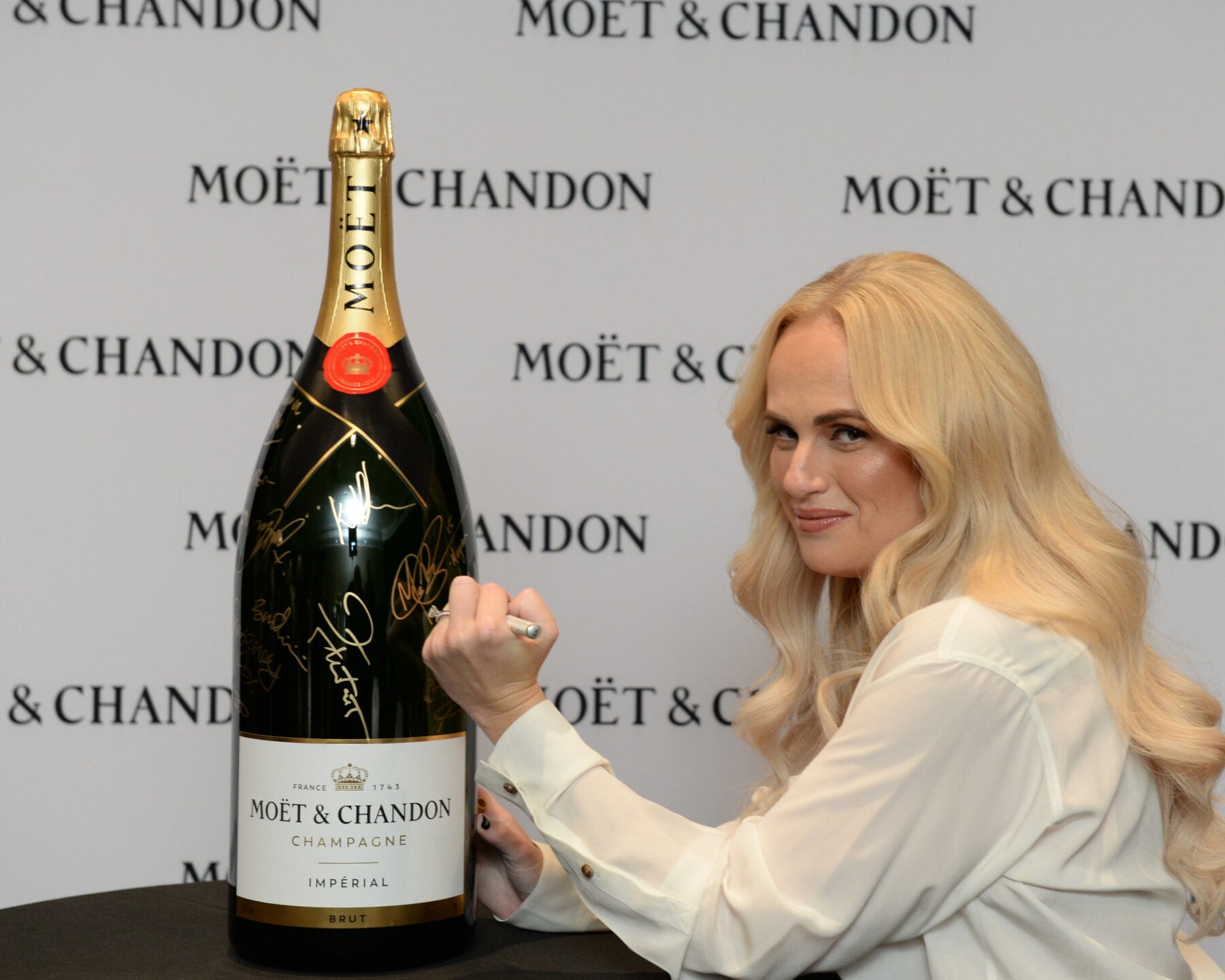 Celebrity woman with long blonde hair holding a large Moët & Chandon champagne bottle at TIFF event.