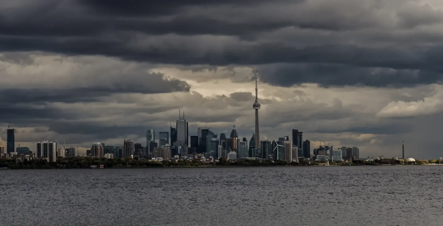 Toronto skyline under dark stormy clouds with the CN Tower visible over Lake Ontario.