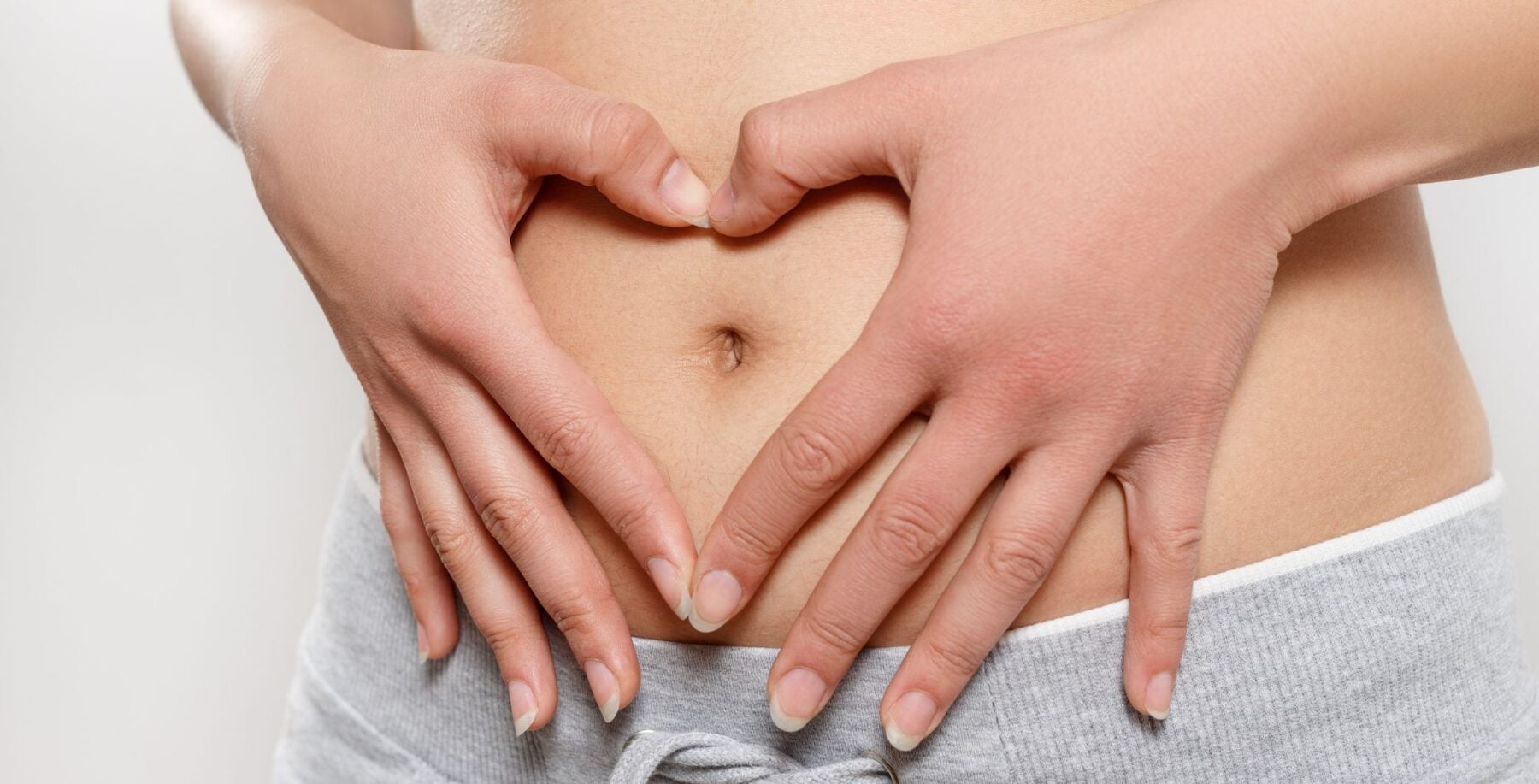 Close-up of a woman's midsection with hands forming a heart shape over her stomach, emphasizing health and wellness.