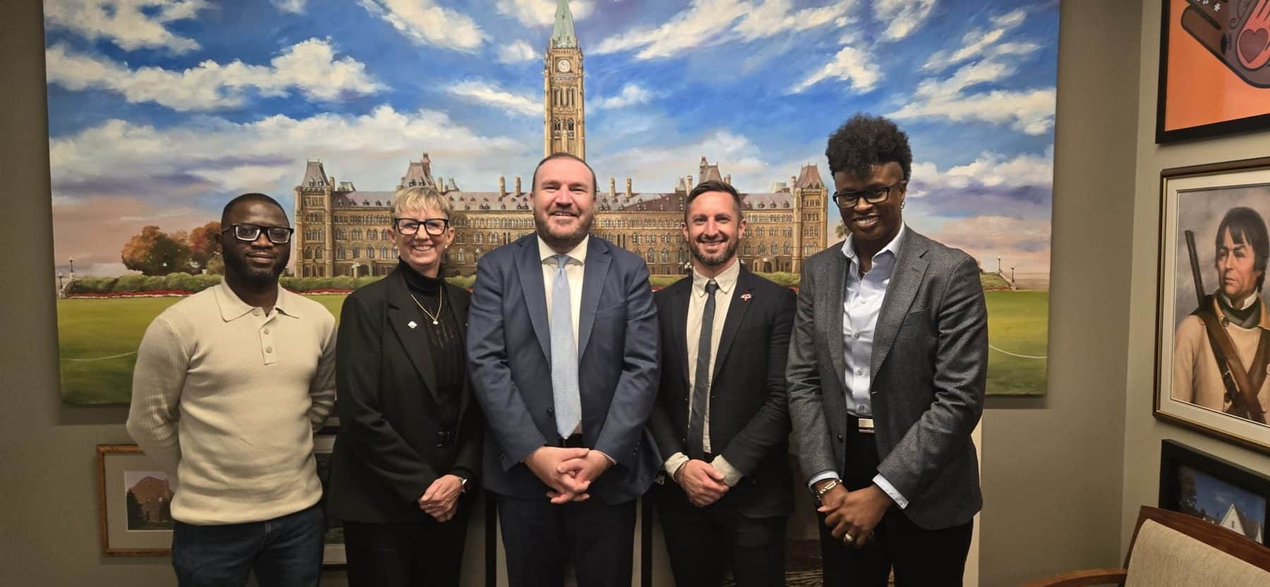 Group of five diverse individuals standing in front of a Parliament Hill painting at a 2SLGBTQIA+ event in Ottawa.