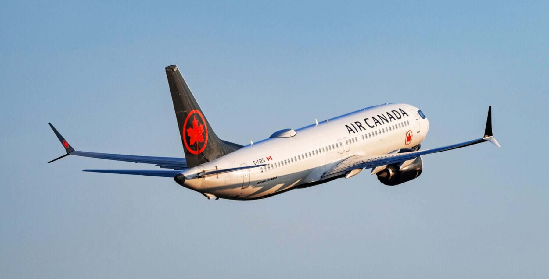 Air Canada commercial airplane flying in clear blue sky, showcasing airline branding and modern aircraft design.