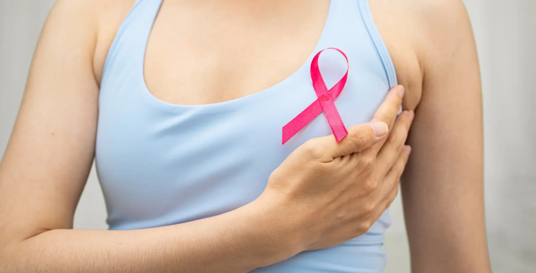 Woman wearing a light blue top with a pink breast cancer awareness ribbon on her chest.
