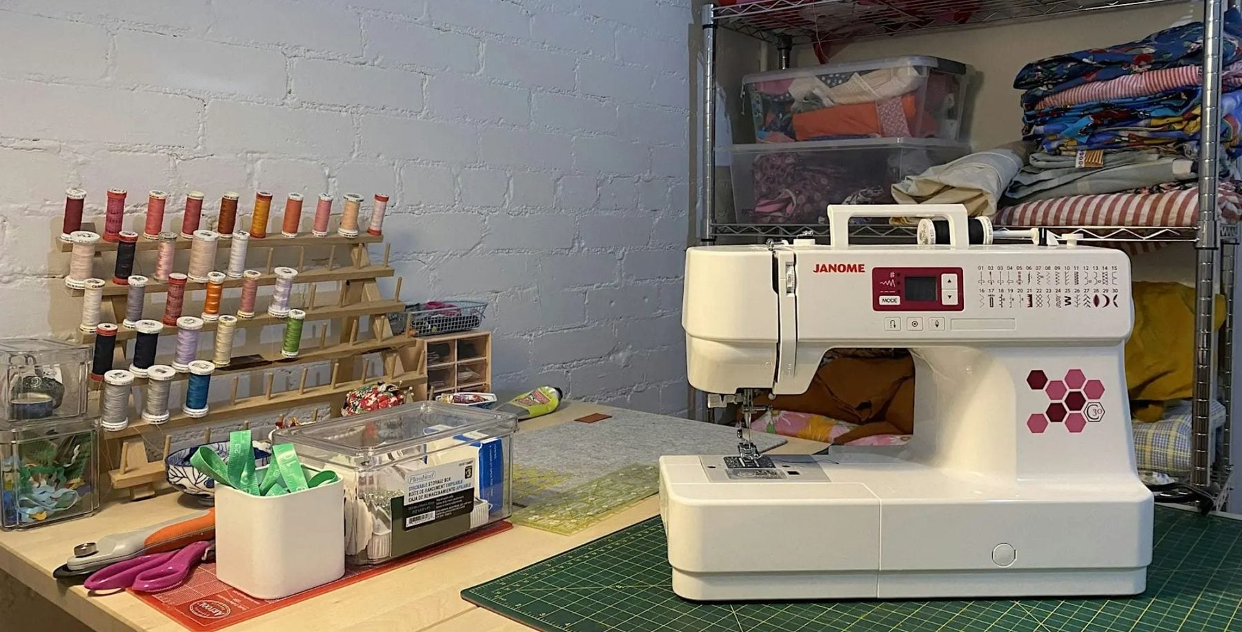 Sewing machine on a work table with spools of thread and fabric supplies in the background.