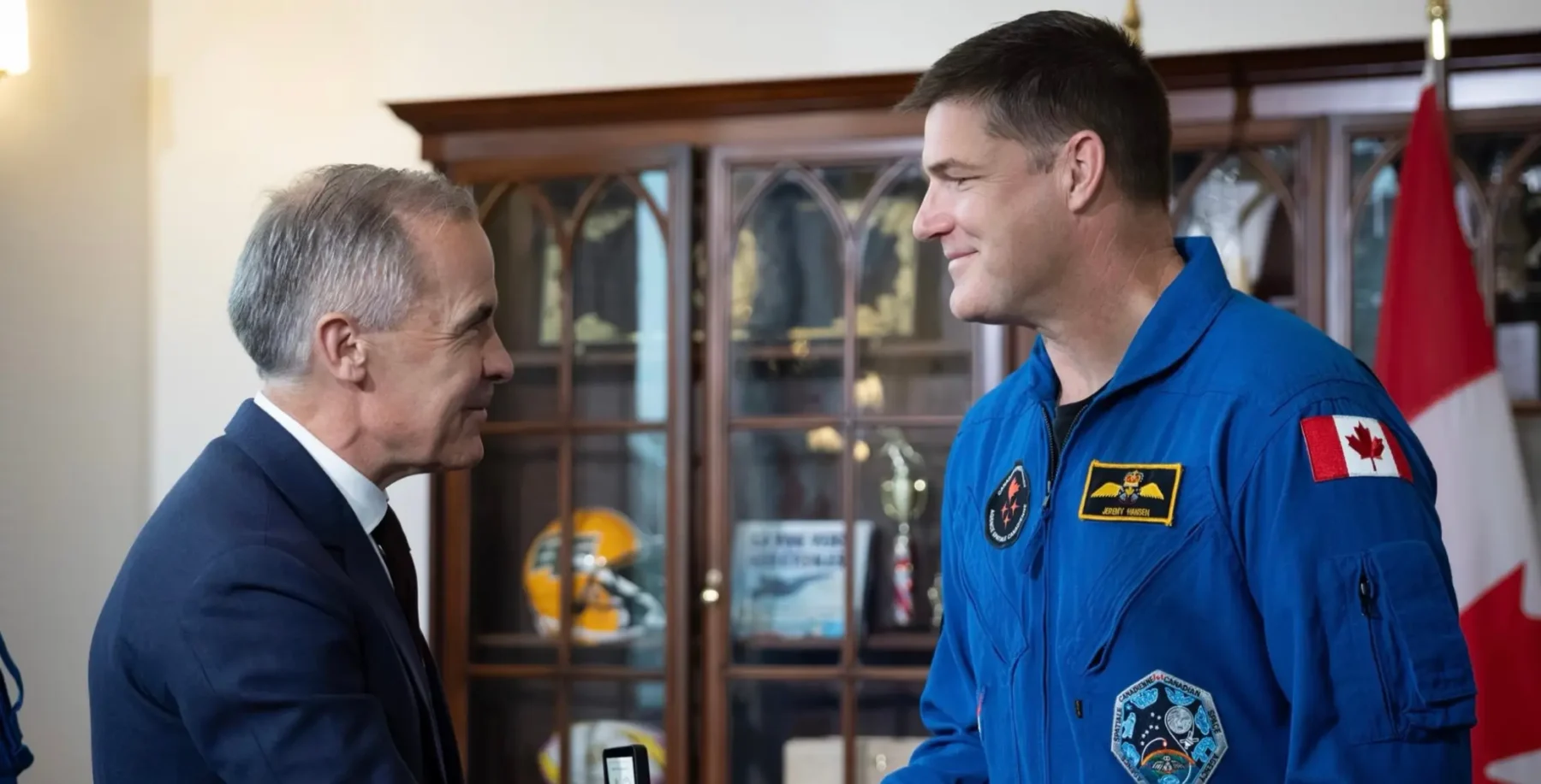 Astronaut Jeremy Hansen in blue space suit with Canadian flag, smiling and shaking hands with an older man in a suit in a formal setting.