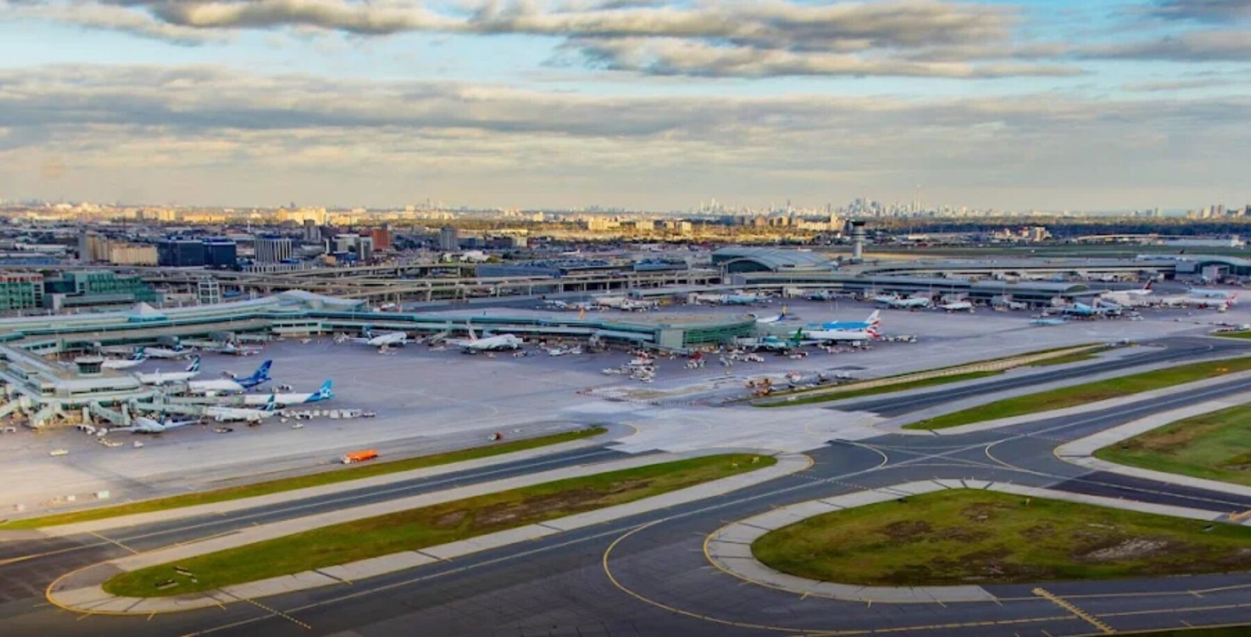 Toronto Pearson Airport with multiple airplanes parked and taxiways visible under a partly cloudy sky.