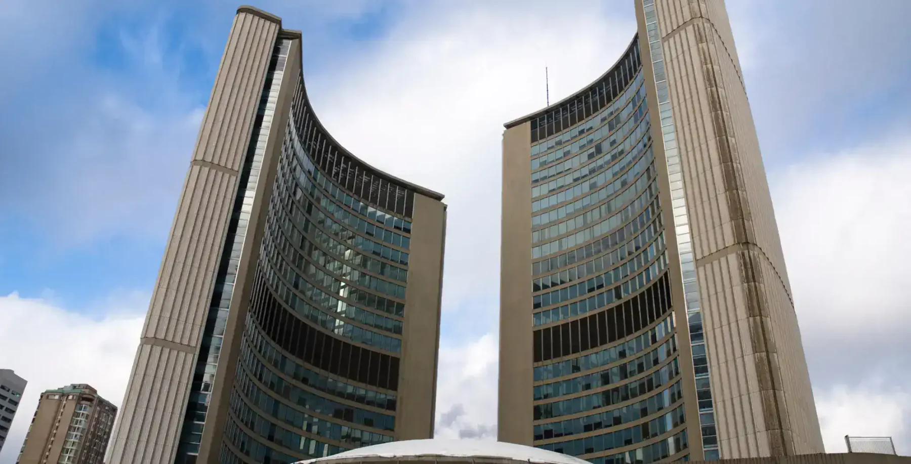 Toronto City Hall twin curved towers seen from below, blue sky with light clouds.