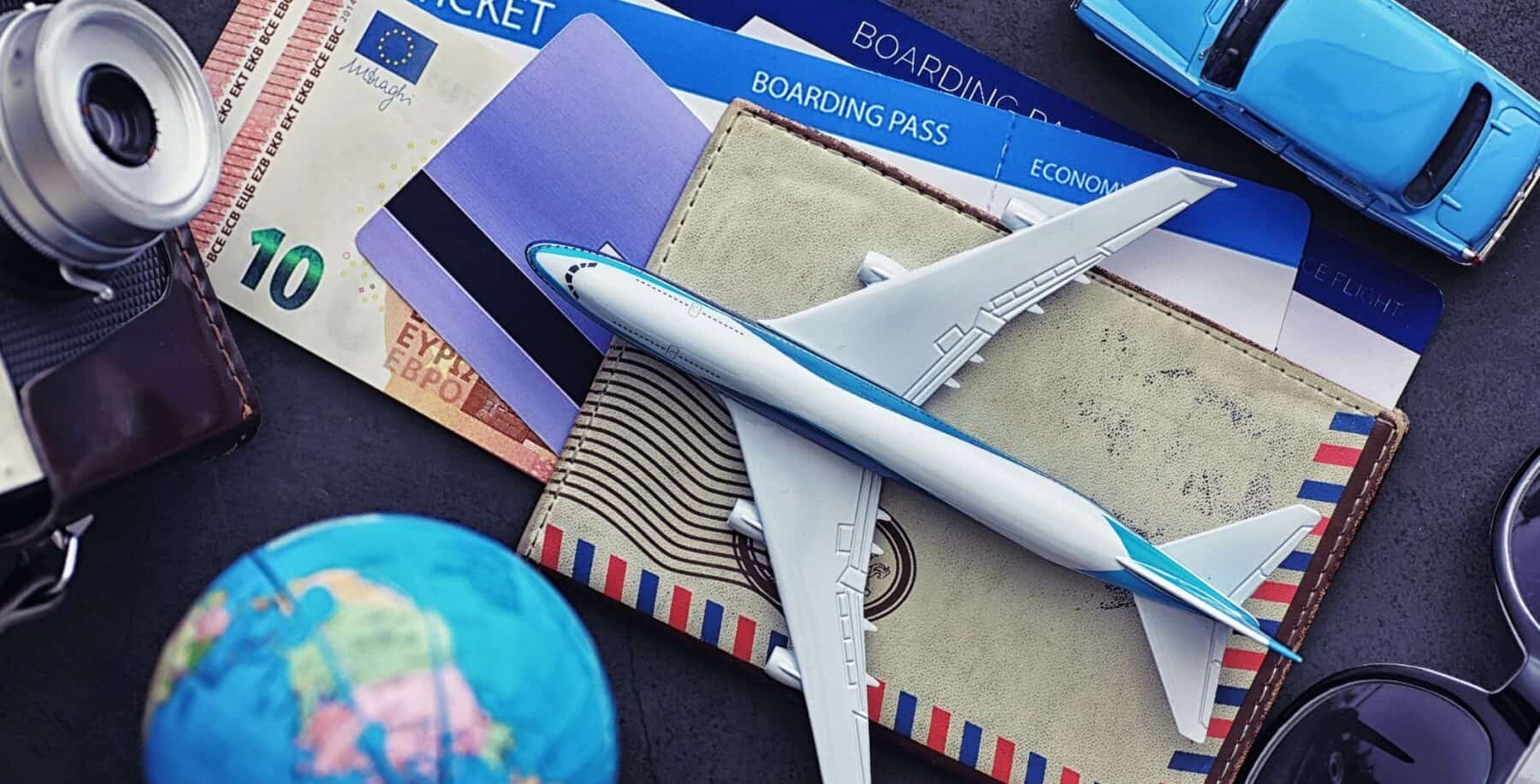 Travel essentials including a toy airplane, boarding passes, a globe, and a toy car, arranged on a dark surface, representing travel planning for Thanksgiving weekend.