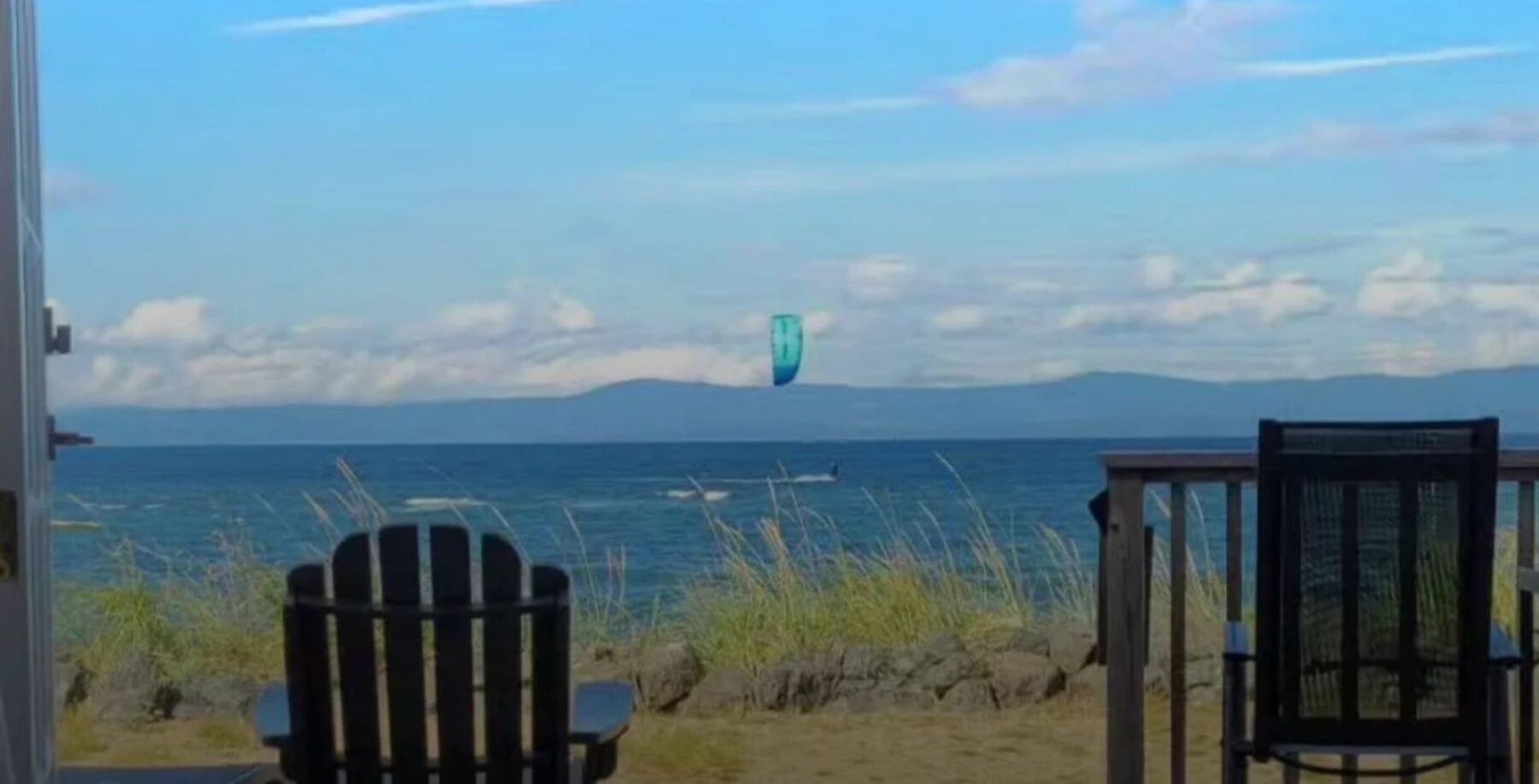 Scenic view of the ocean with a kite in the sky, two chairs facing the water, and grassy shoreline, capturing a peaceful coastal landscape in Vancouver Island.