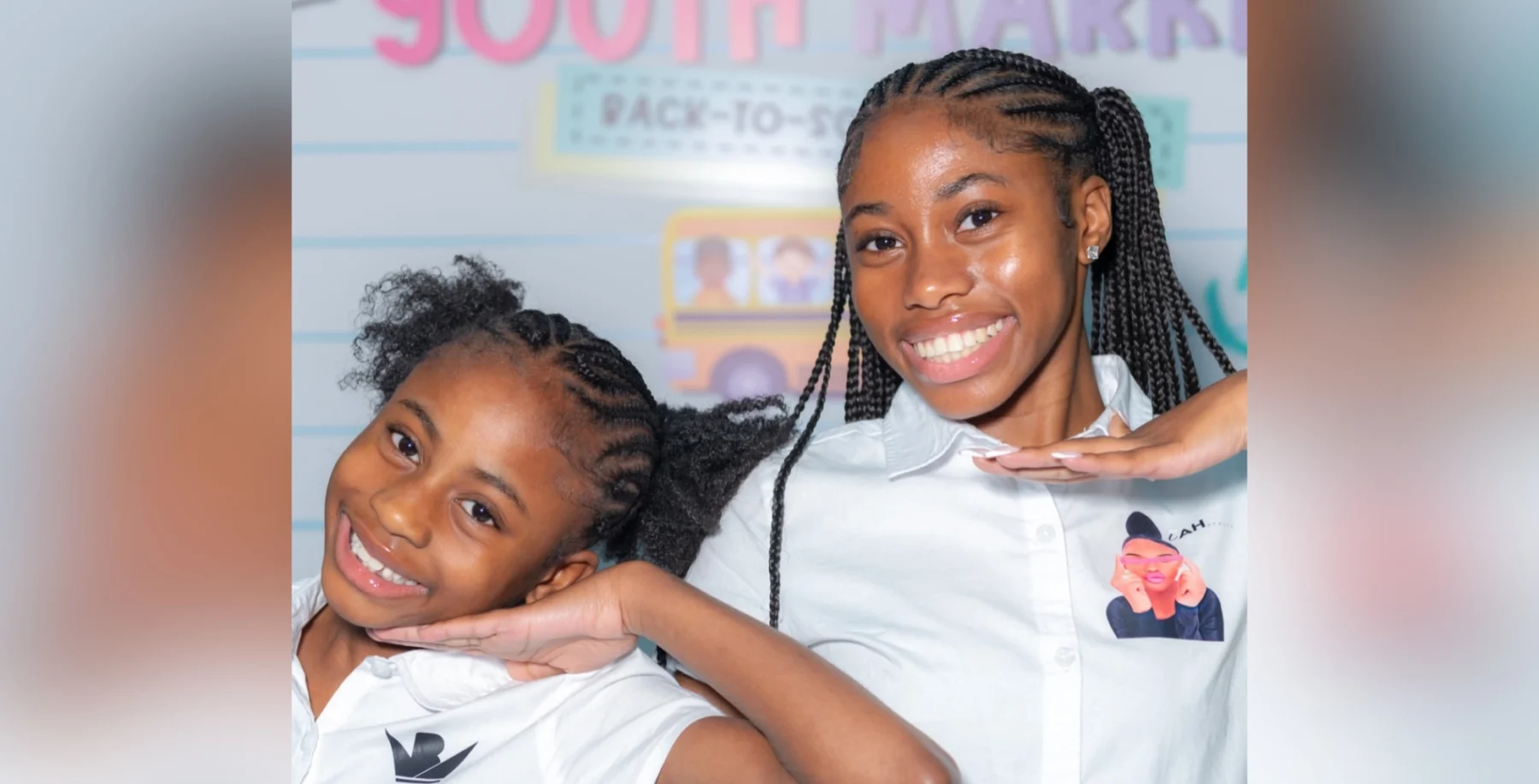 Two smiling sisters posing gracefully, wearing white uniforms with name badges, in front of a blurred backdrop with a bold sign in pink text.