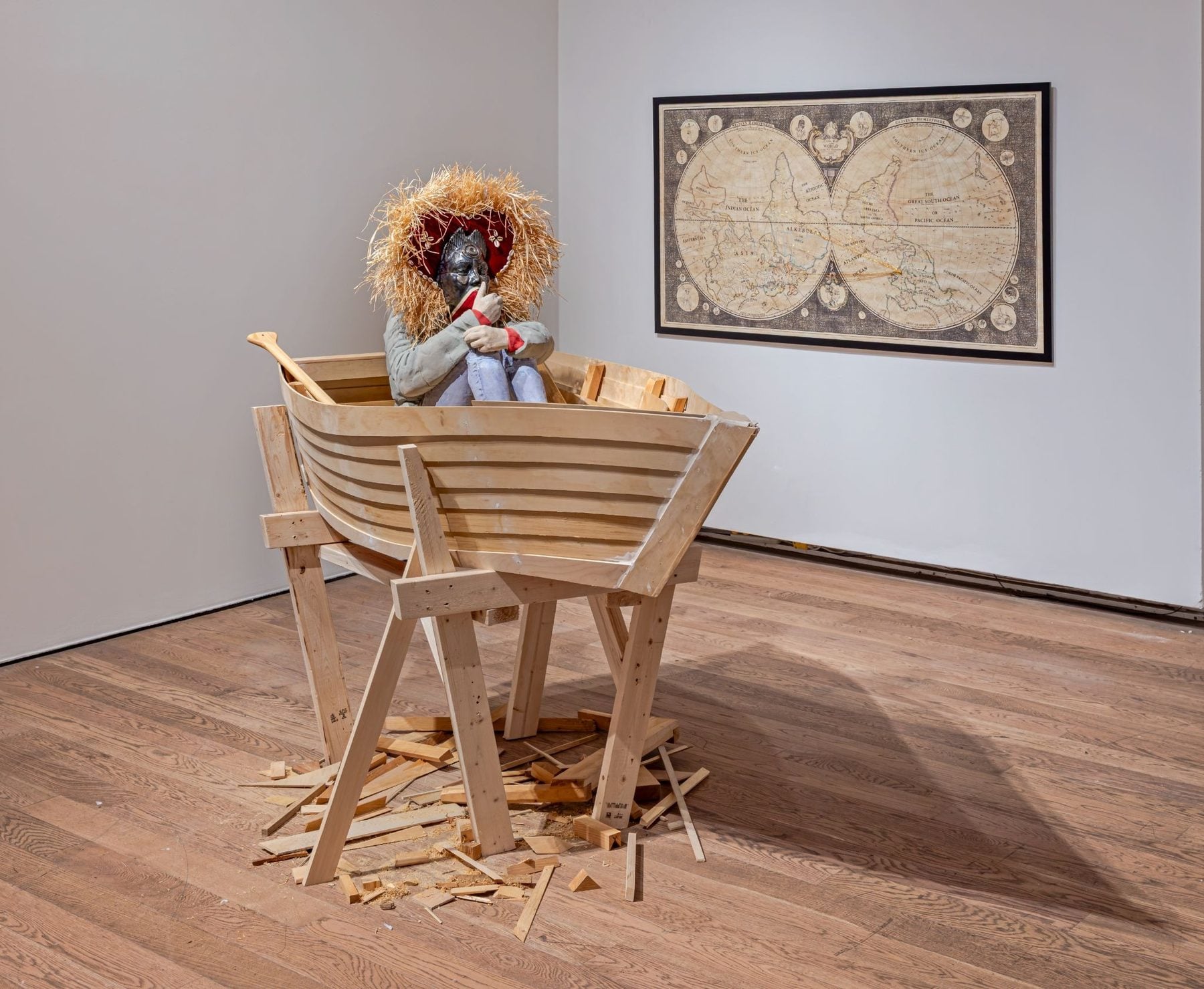 NOW Toronto exhibit at Gardiner Museum featuring a wooden barricade sculpture with a humanoid figure wearing a straw hat, against a map artwork on the wall.