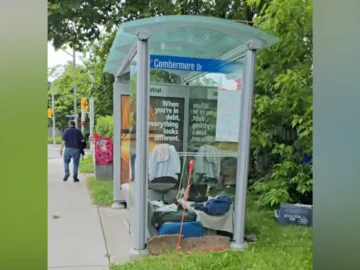 Bus stop shelter in Toronto with belongings and advertising, green foliage background, city street scene.