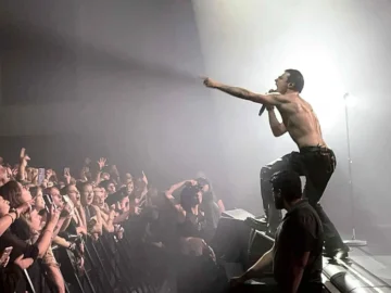 Vibrant concert scene with a shirtless male performer engaging energetic audience with fans and smartphones, spotlight illuminating stage and crowd at a live music event in Toronto.