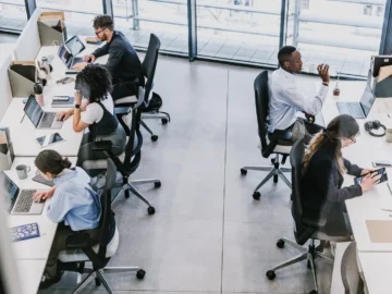 Modern Toronto office workspace with diverse professionals working on laptops and tablets, featuring large windows with city views, technology, and coworking environment.