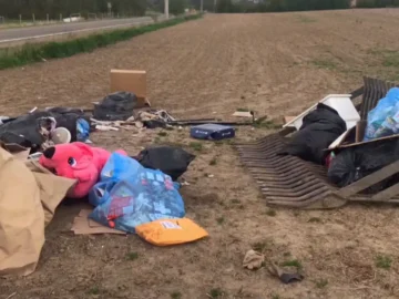 An image showing scattered garbage, including bags, boxes, and household items, in a rural area following a dumping incident.